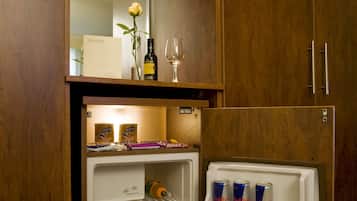 A hotel room with a minibar, a refrigerator stocked with beverages, and a wooden cabinet.