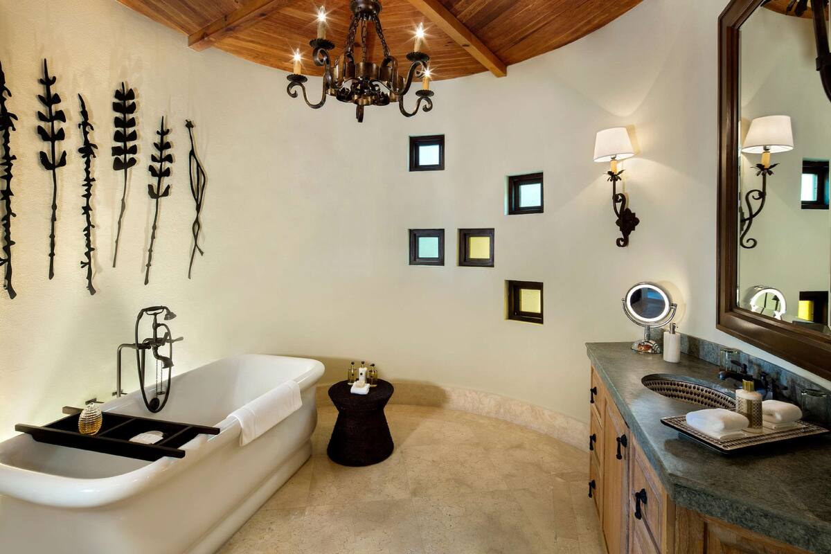 Un baño con bañera, tocador con espejo, luces empotradas y candelabro.