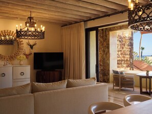 Ein Wohnzimmer mit Sofa, Fernseher, Wanddekoration und Blick auf den Strand durch eine offene Tür.