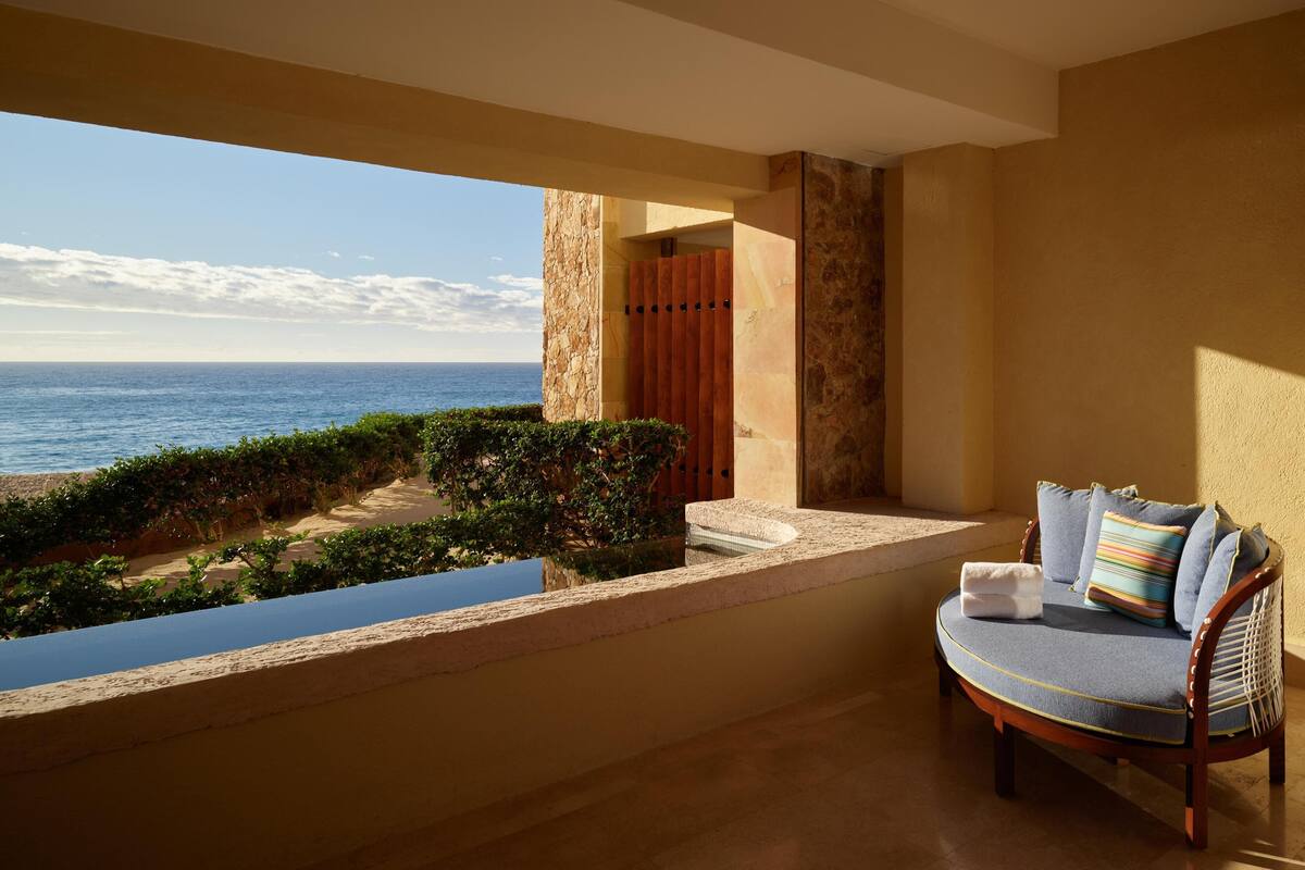Un balcón con vista al mar, una silla con cojines y un muro de piedra.