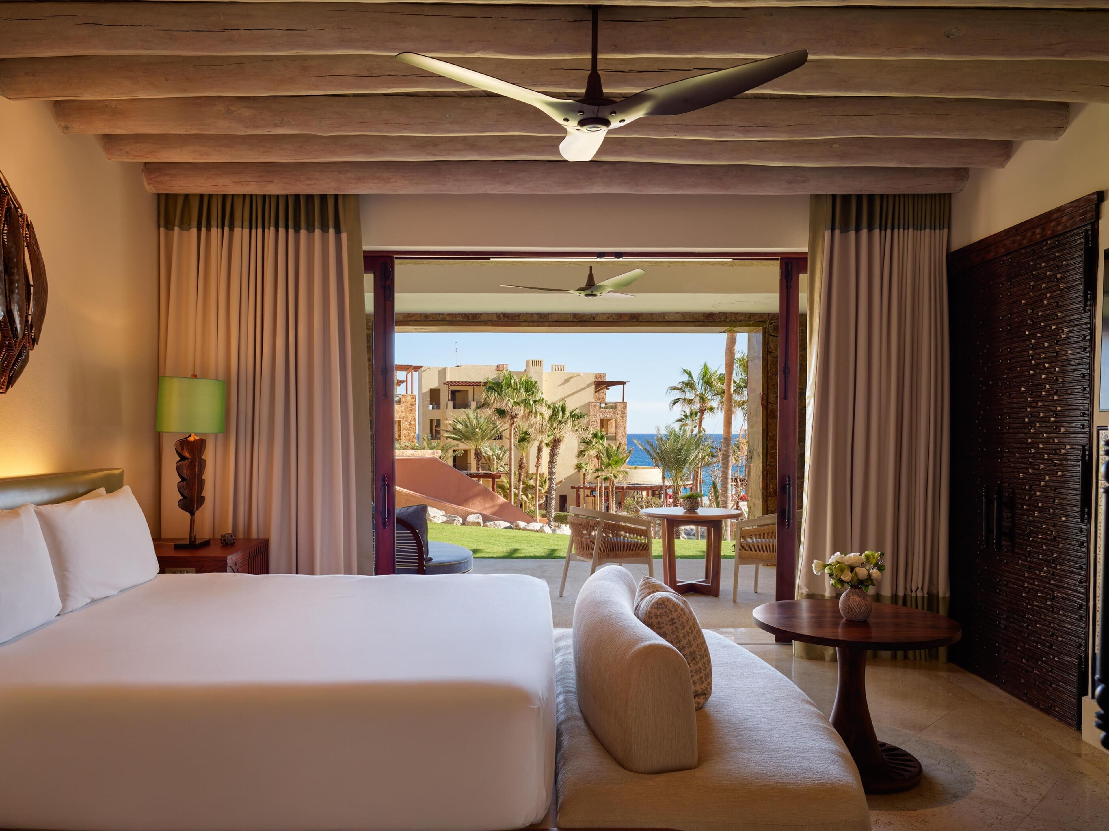 Habitación de hotel con una cama grande, un sofá, una mesa con un jarrón y vistas a la piscina y edificios.