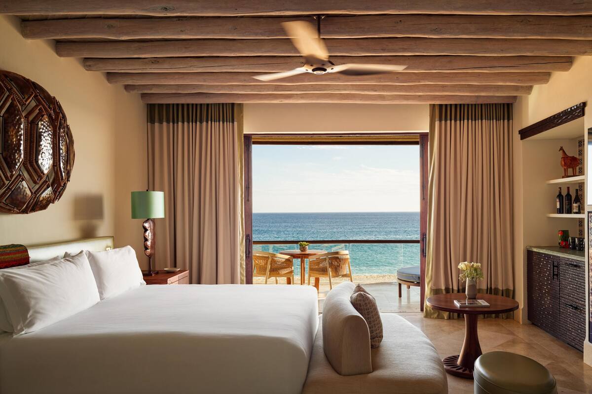 Habitación de hotel con una cama grande, un sofá, una mesita y un balcón con vista al mar.