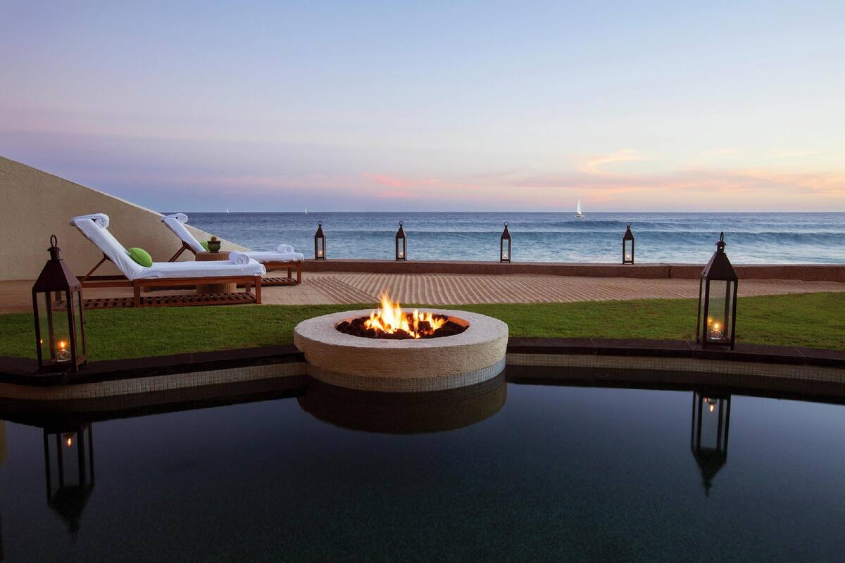 Zona junto a la piscina con sillones, una fogata y vista al océano.
