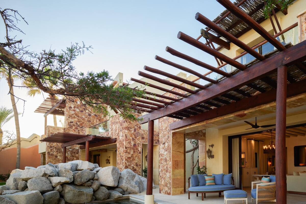 Zona de piscina con pérgola, paredes de piedra y mobiliario exterior.
