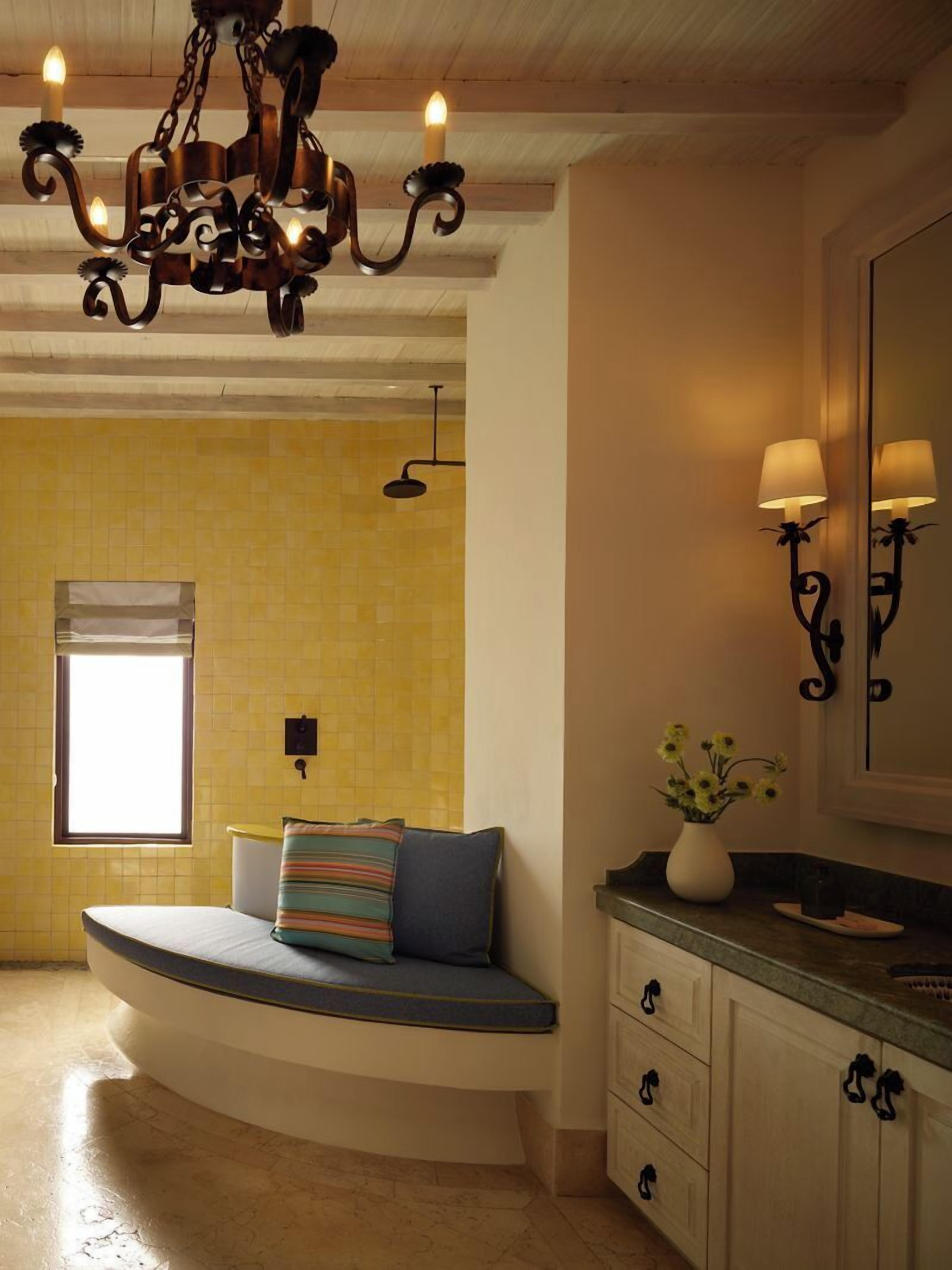 A bathroom with a curved bench, a chandelier, a mirror, and a window.