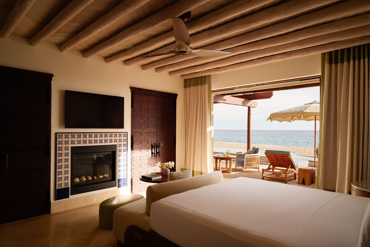 Ein Hotelzimmer mit einem großen Bett, einem Kamin, einem an der Wand montierten Fernseher und Blick auf den Strand.