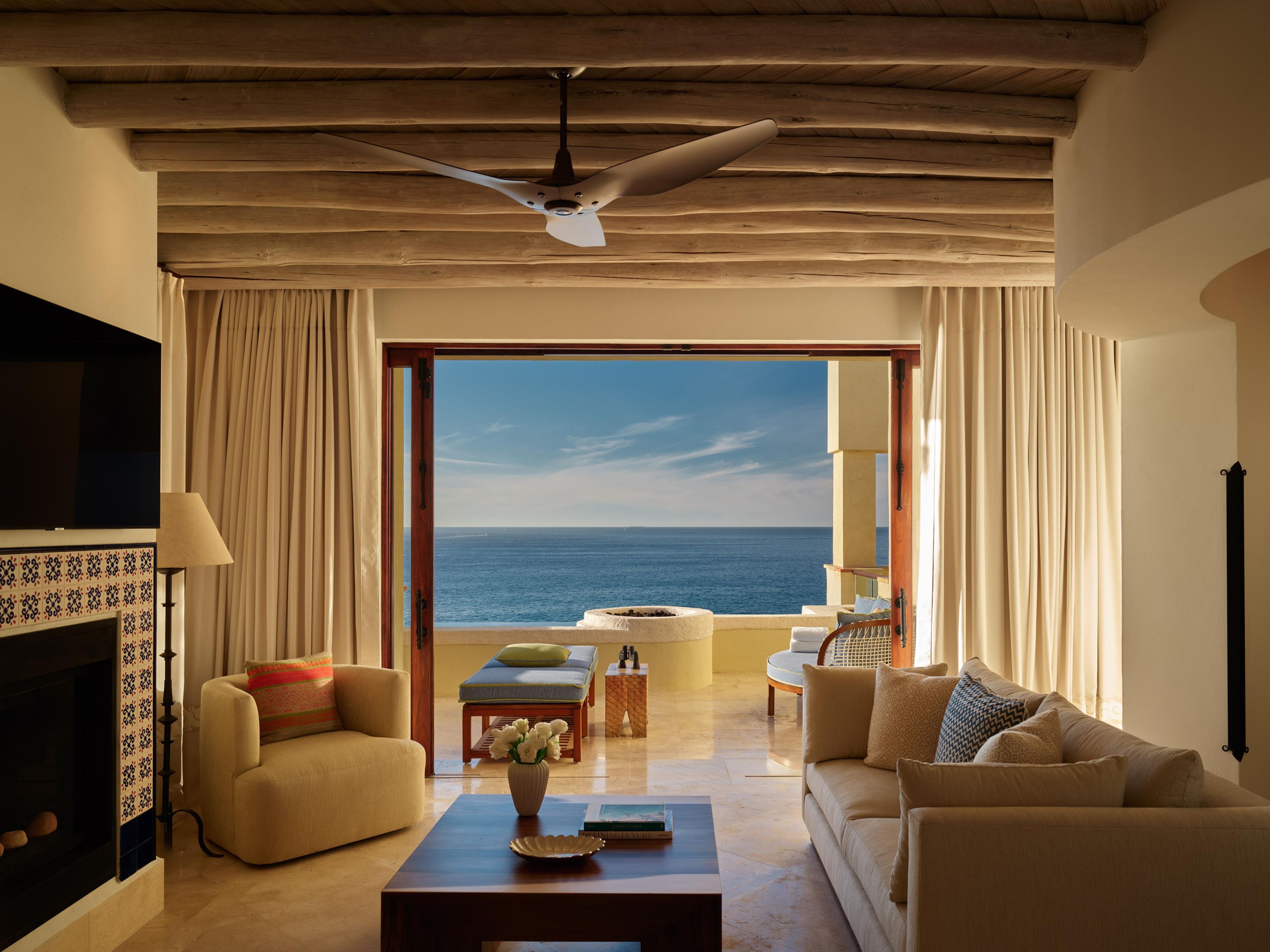 A spacious living room with a view of the sea, a fireplace, and a ceiling fan.