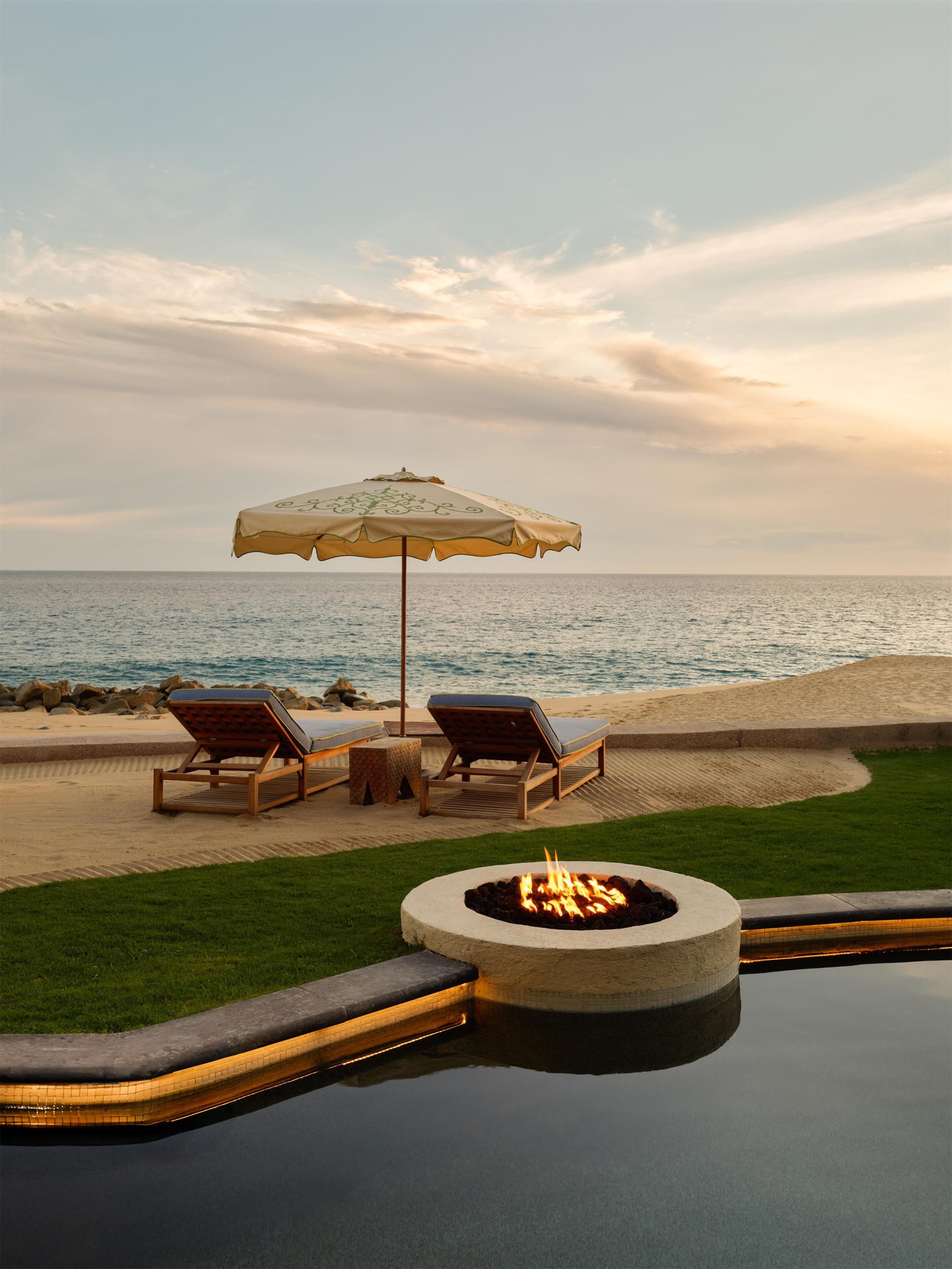 A beachside pool area with lounge chairs and an umbrella, overlooking the ocean.