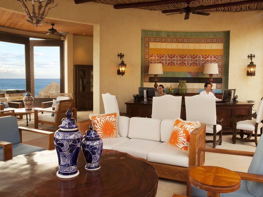 Een ruime zithoek met een grote bank, meerdere stoelen, een houten tafel en uitzicht op de oceaan.