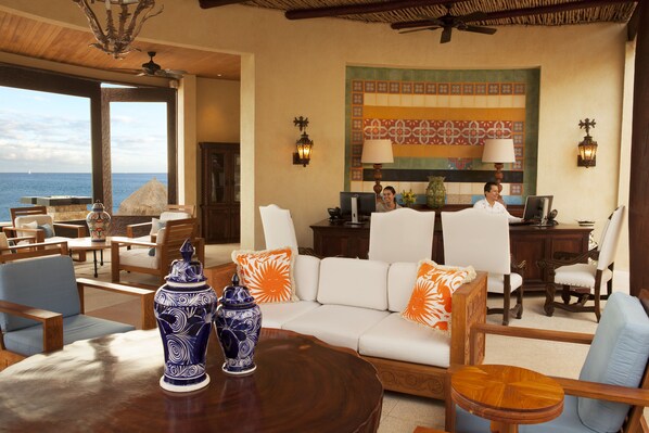 A spacious lounge area with a large sofa, multiple chairs, a wooden table, and a view of the ocean. - Waldorf Astoria Los Cabos Pedregal (Cabo San Lucas)