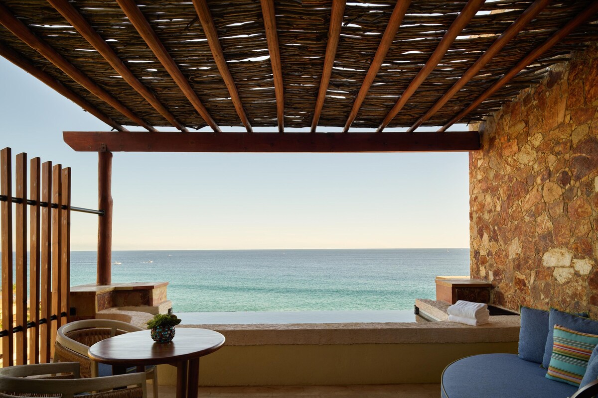 Eine Terrasse mit Blick aufs Meer, Holzmöbel und eine Steinmauer.