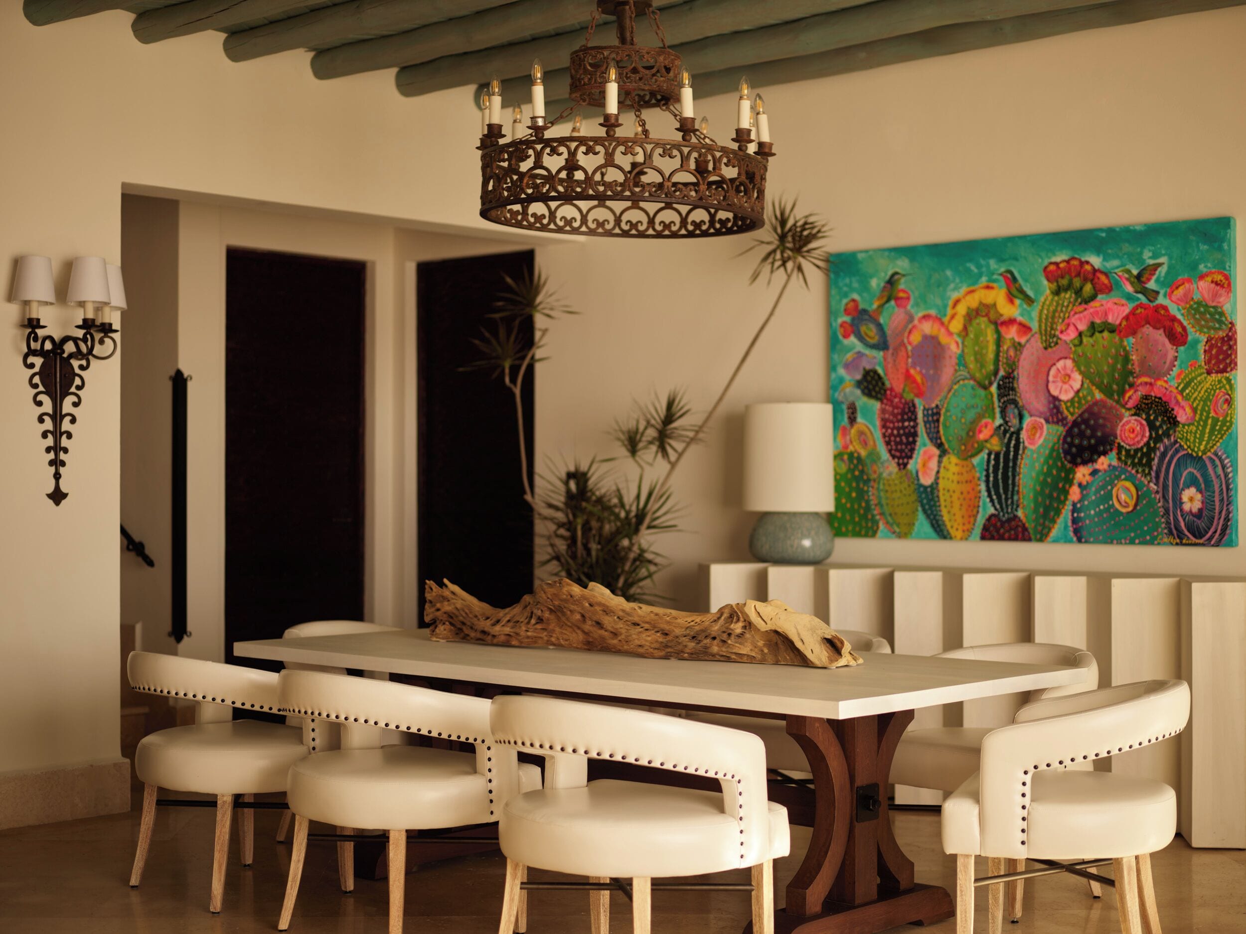 A dining area with a chandelier, a cactus-themed painting, and a table with chairs.