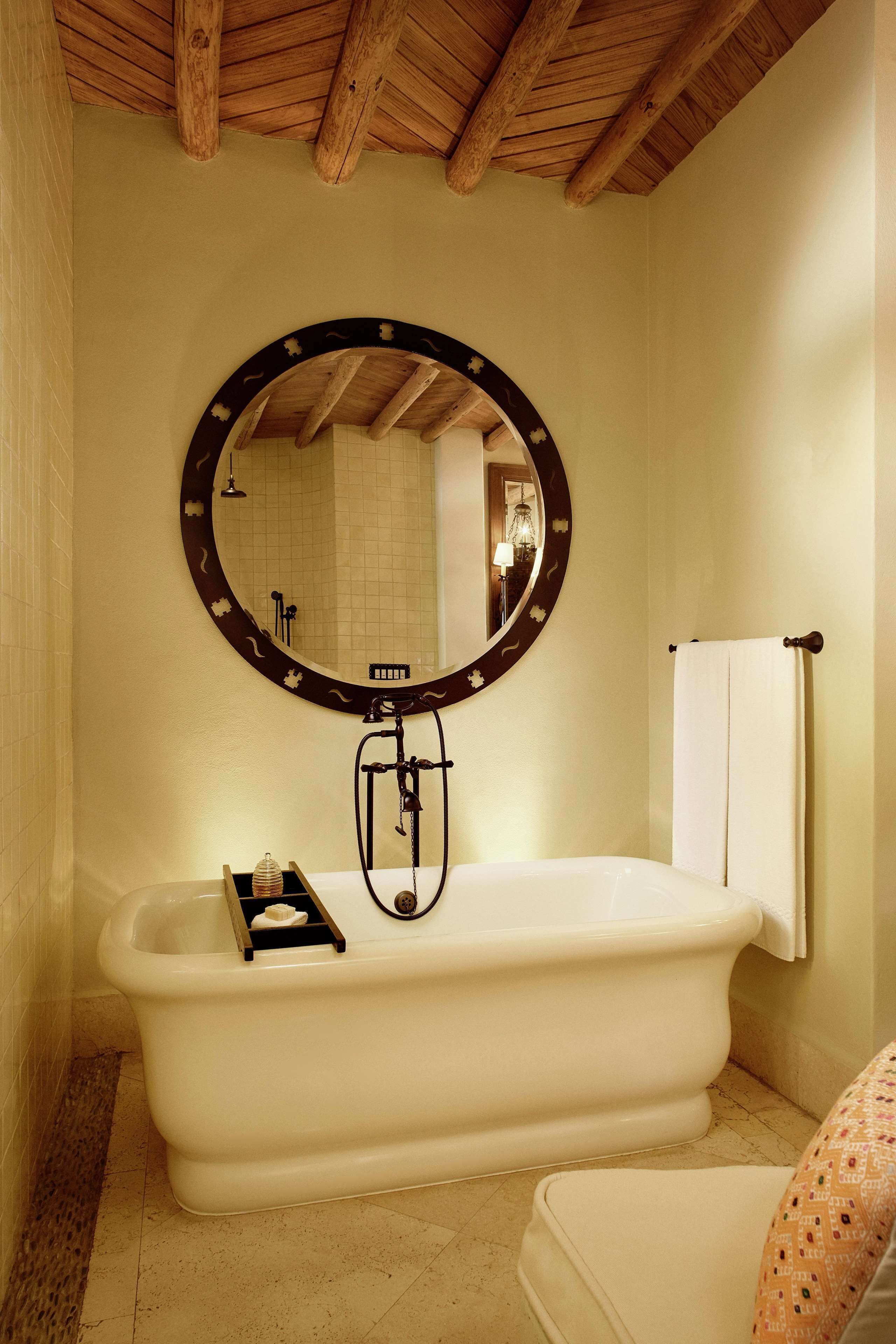 Un baño con una bañera independiente, un espejo redondo con marco decorativo y un perchero para toallas.