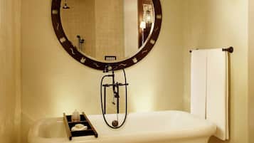 Un baño con una bañera independiente, un espejo redondo con marco decorativo y un perchero para toallas.