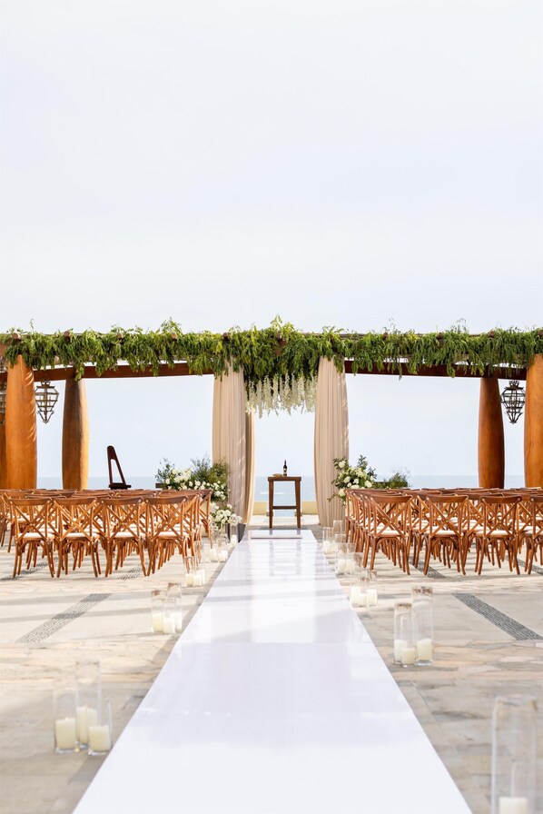 Une cérémonie de mariage organisée sur la plage, avec une allée blanche, des chaises en bois et un autel en bois.