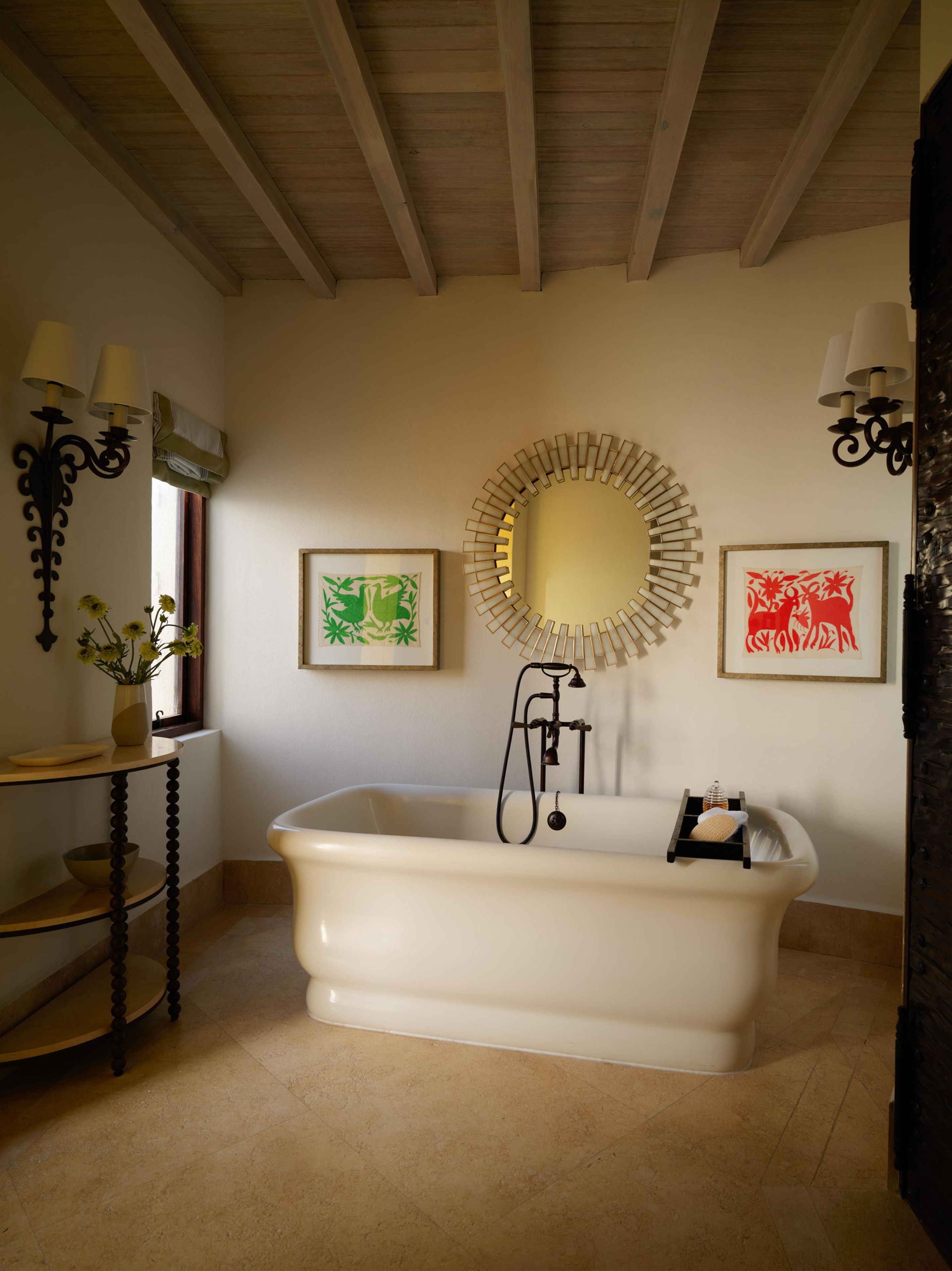 Een badkamer met een vrijstaand bad, een ronde spiegel en twee kunstwerken in lijsten aan de muur.