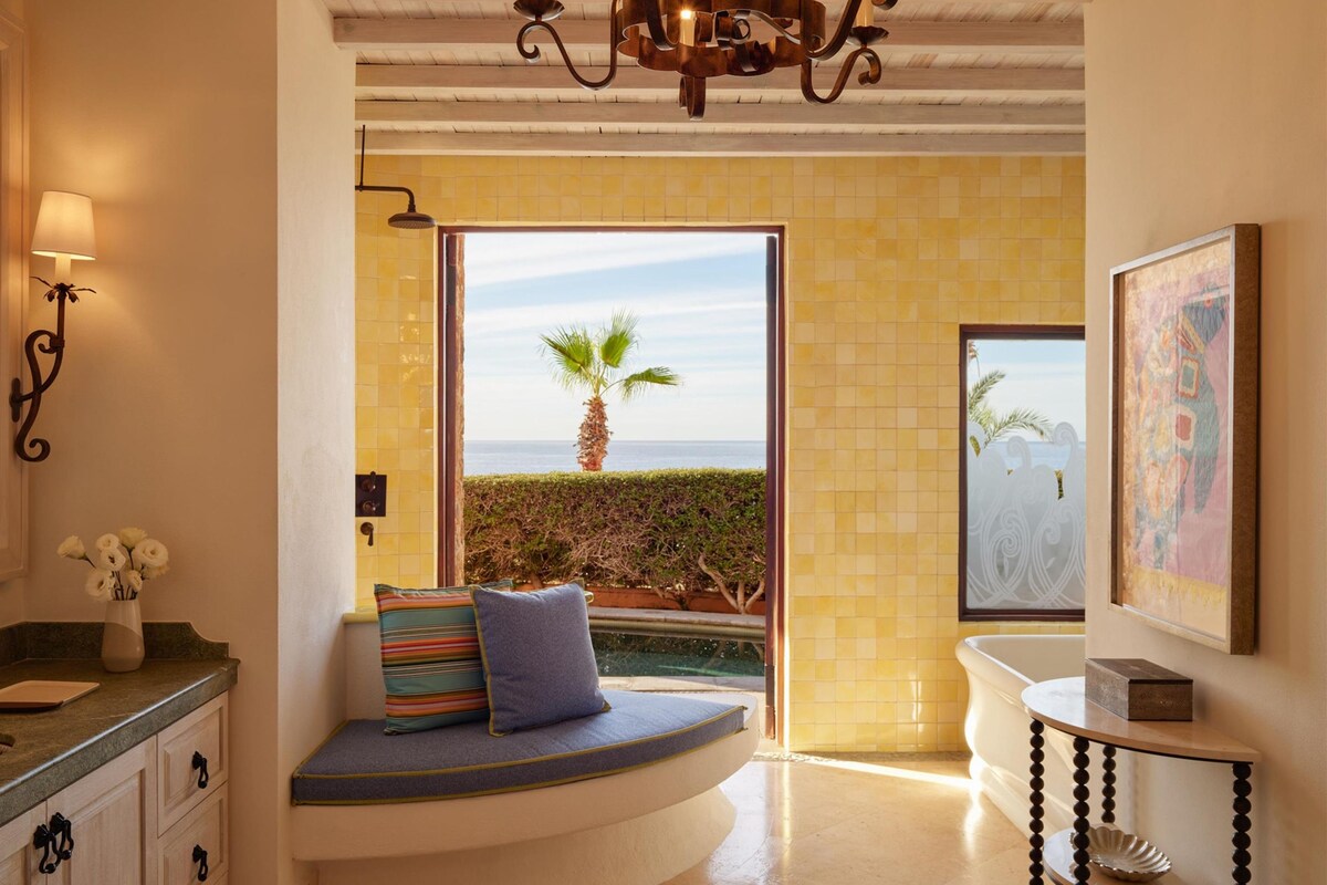 Ein modernes Badezimmer mit einer Badewanne, einer Sitzbank mit Kissen, einem Waschtisch mit Spiegel und einer Chandelier.