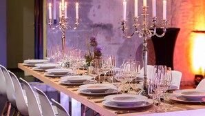 Una larga mesa de comedor dispuesta con platos, copas y velas, indicando una configuración formal para cenar.