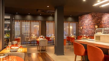 A modern restaurant with wooden flooring, orange chairs, and a bar area.