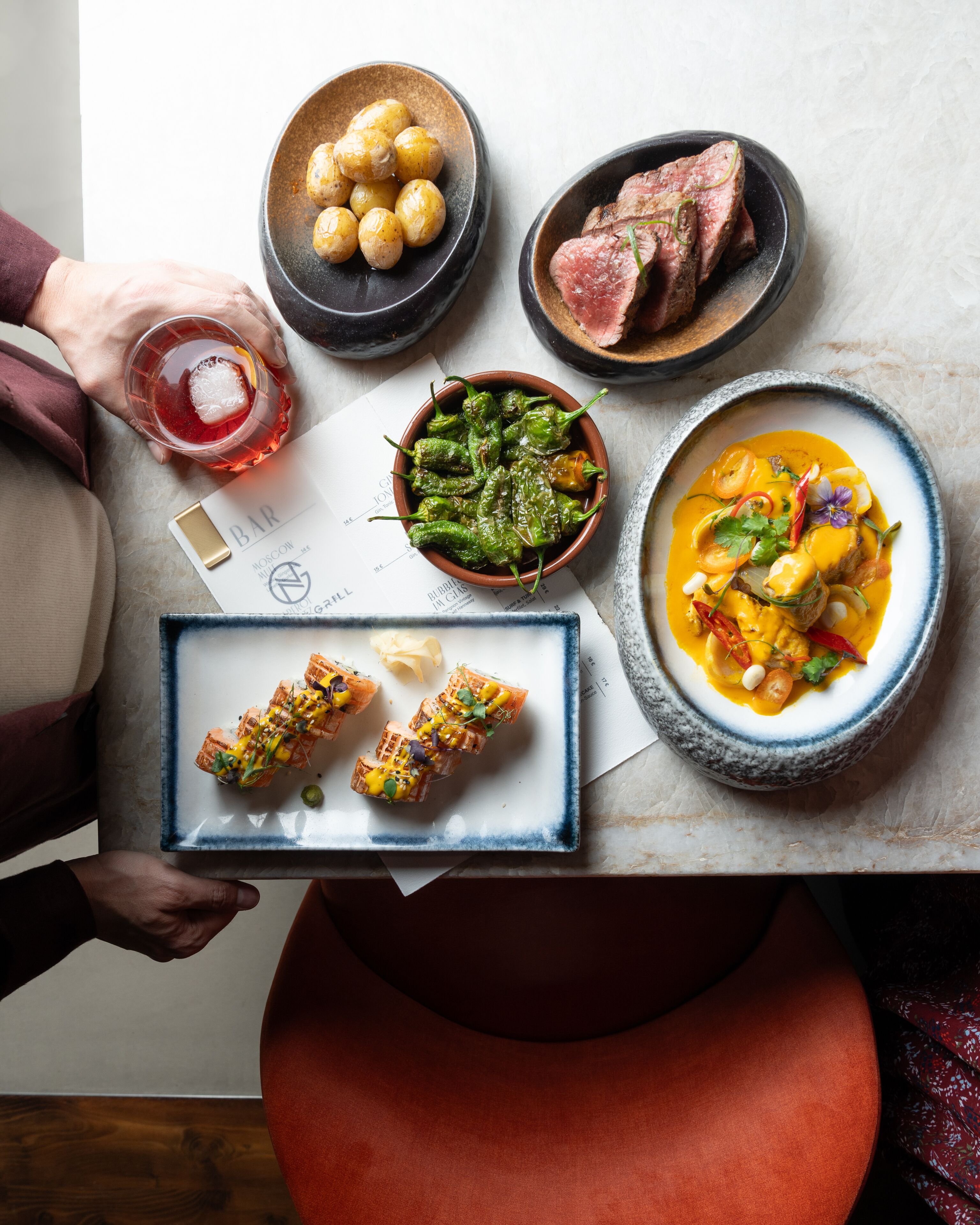 Una mesa con diversos platos, incluyendo un tazón de pimientos verdes, un tazón de papas, un plato de carne asada y un tazón de sopa.