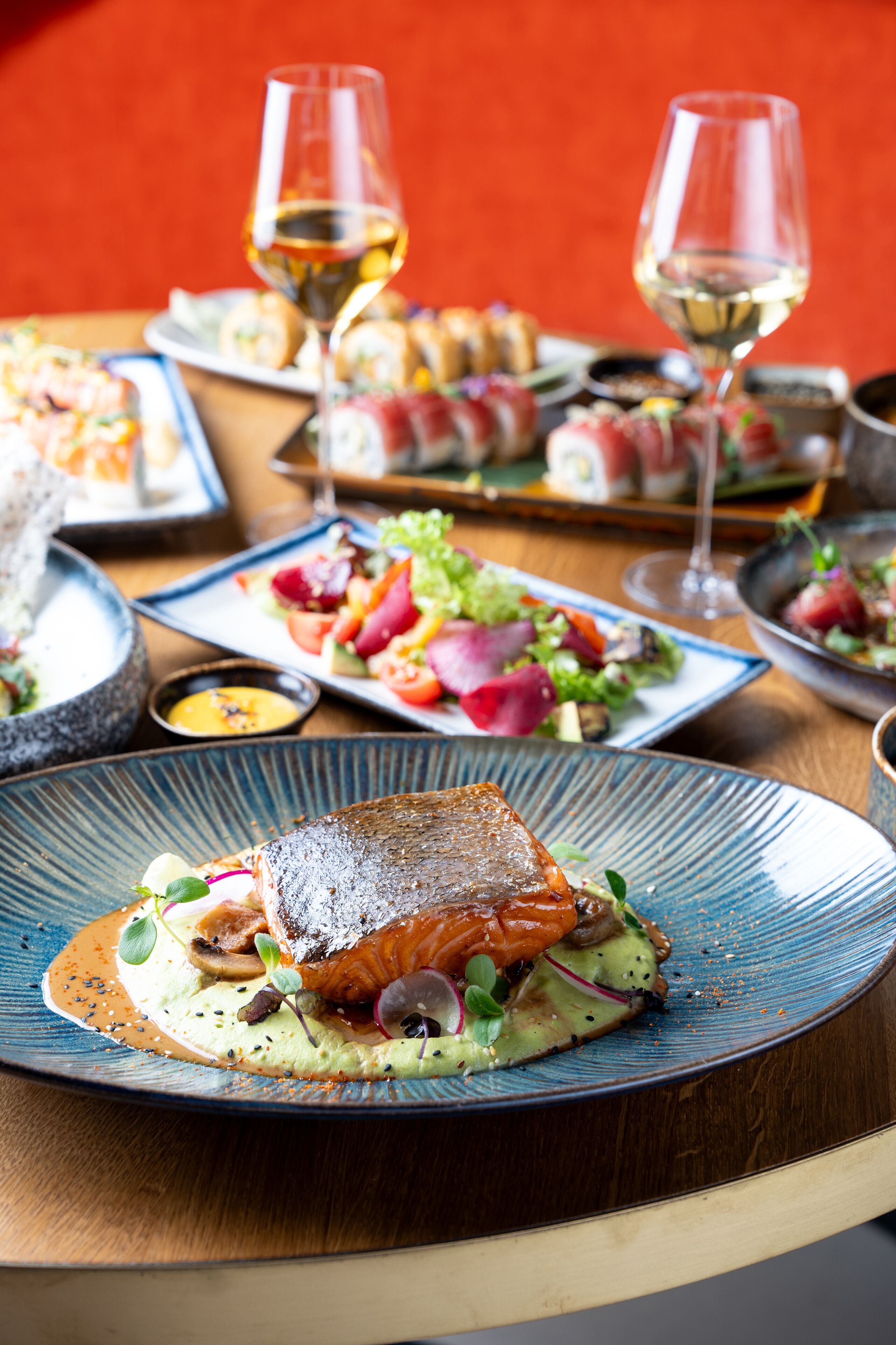 A dining table with various dishes and glasses of white wine.