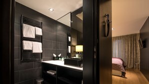 Un baño moderno con una pared de azulejos oscuros, un perchero negro, un lavamanos con artículos de aseo y un espejo.
