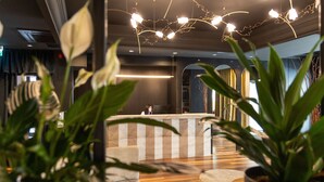 Un área de recepción con mostrador, asientos y plantas en macetas.