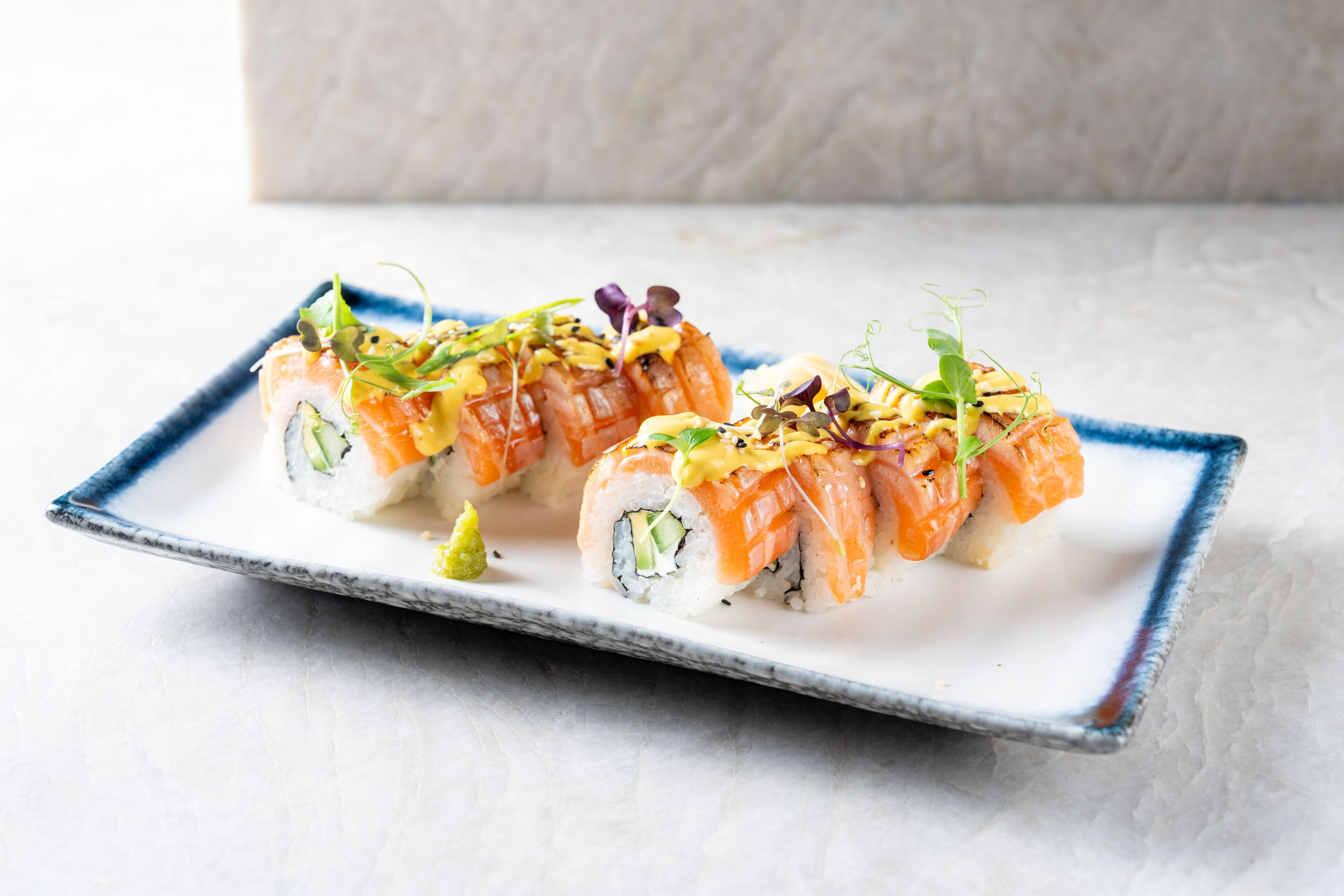 Un plato de sushi con salmón y aguacate sobre un plato de cerámica azul y blanco.