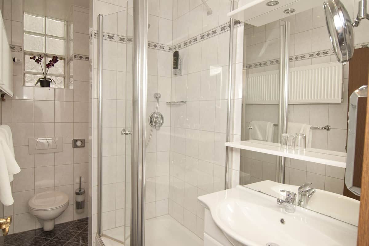 A bathroom with a glass-enclosed shower, a toilet, a sink with a mirror, and a window with flowers.