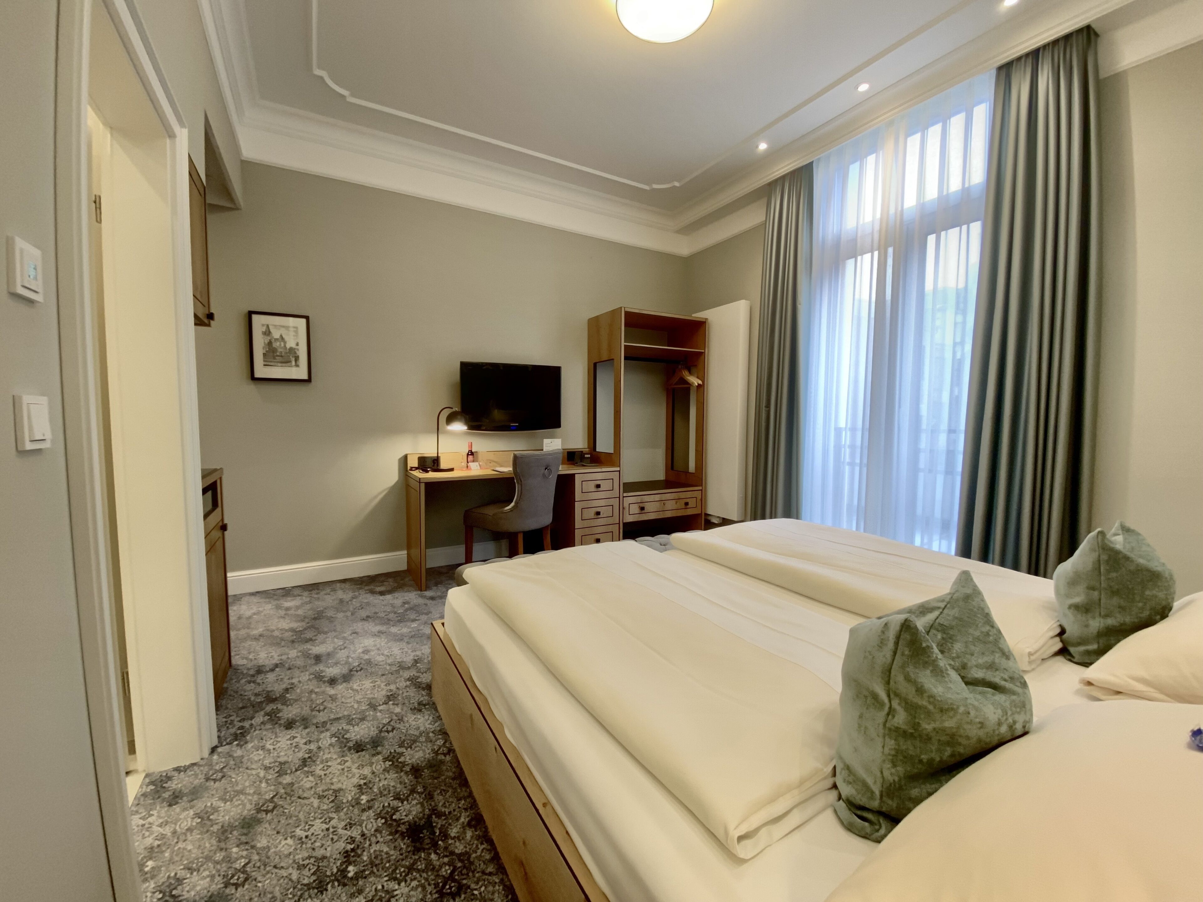 A hotel room with a bed, a desk, a chair, a television, a wardrobe, and a window with curtains.