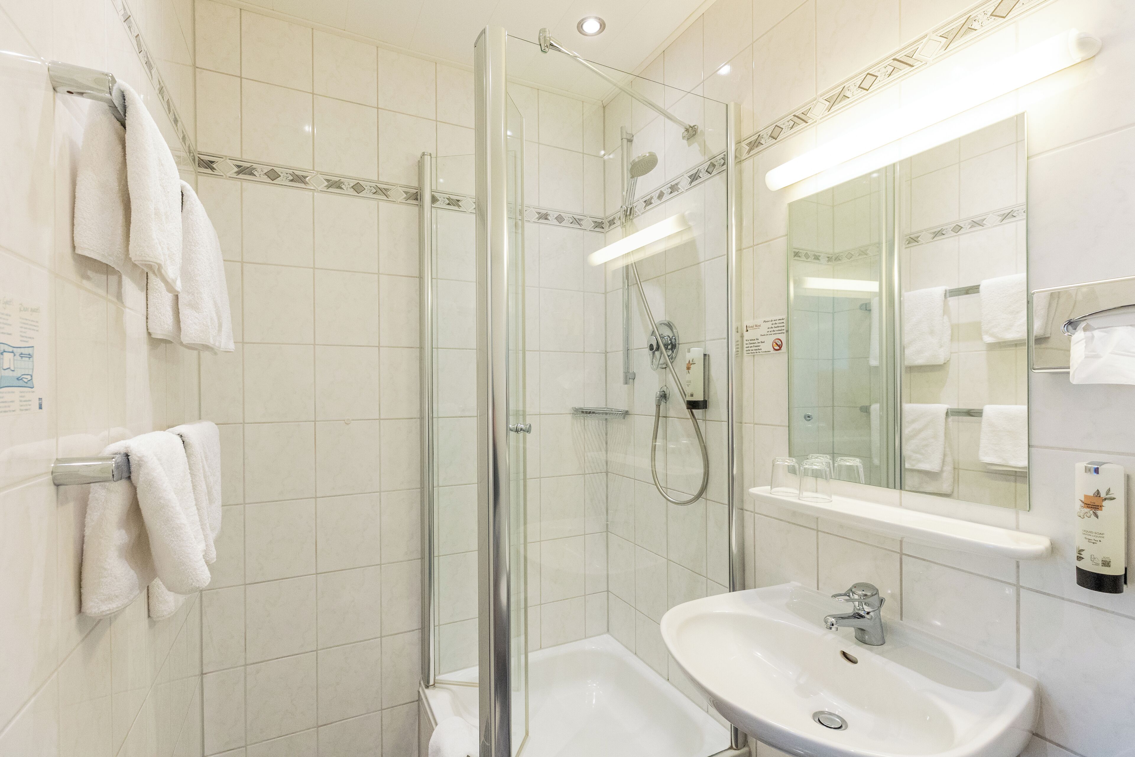 Un bany modern amb dutxa protegida per vidre, un lavabo blanc i un mirall gran.