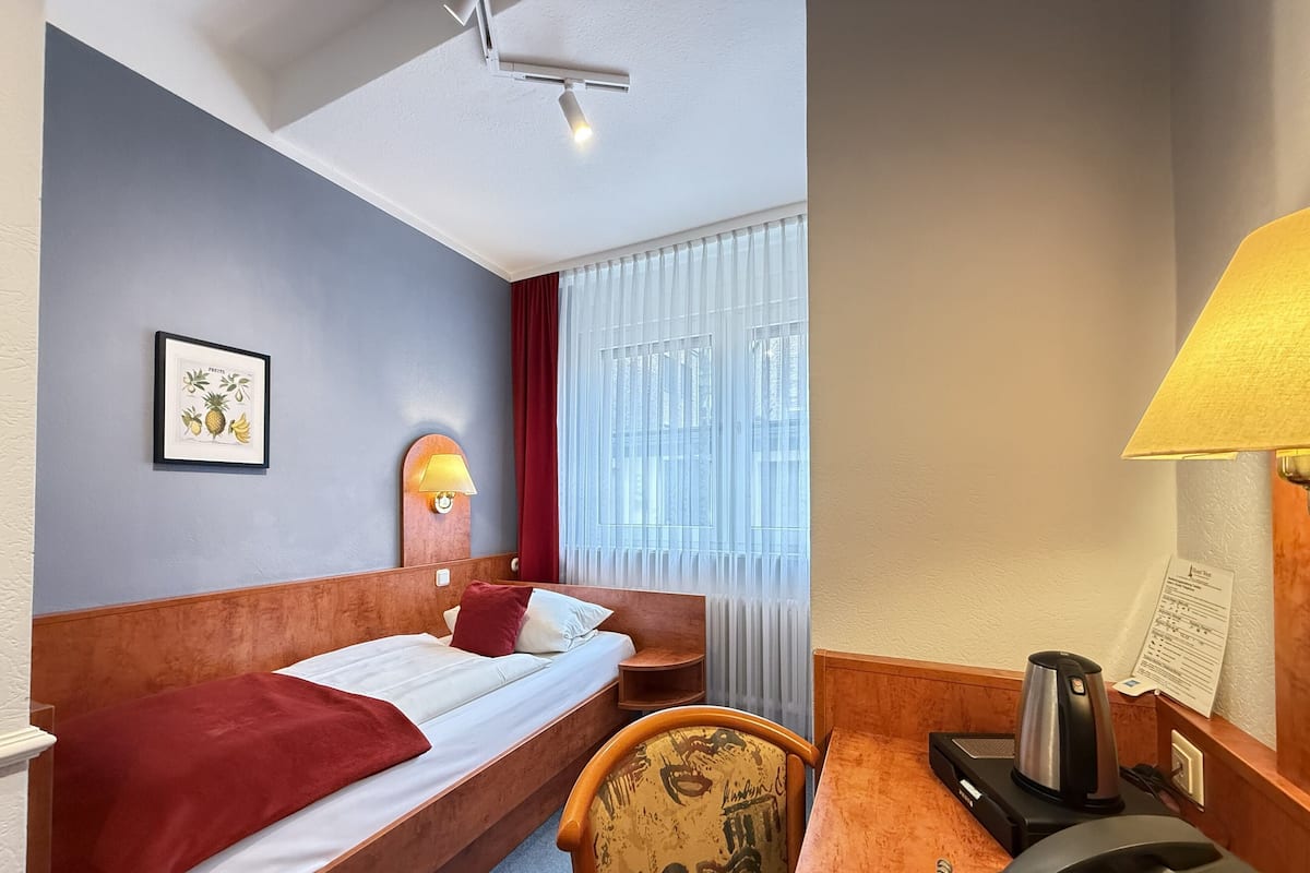 A hotel room with a bed, a desk with a telephone and a coffee maker, a chair, a picture on the wall, and a window with curtains.