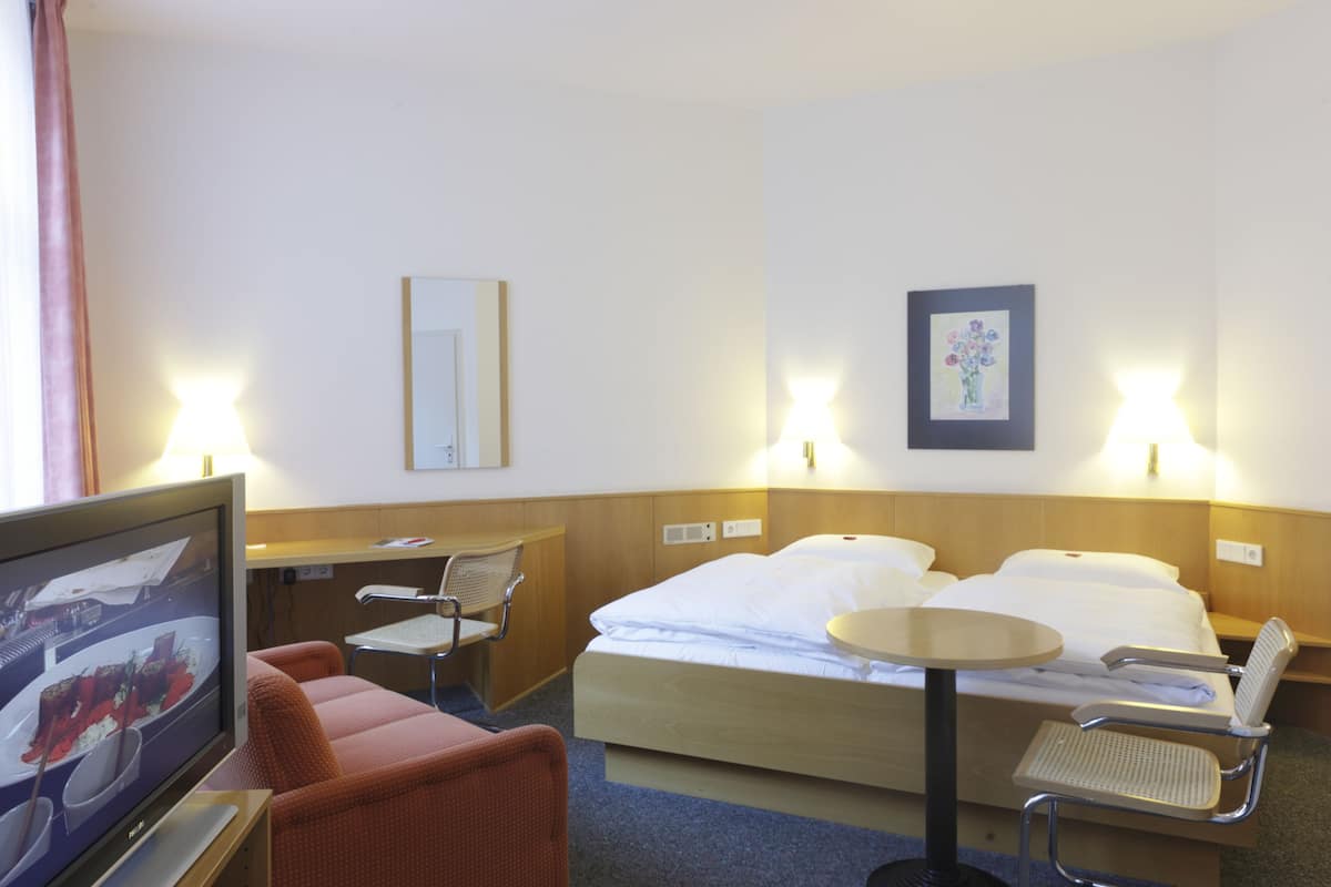 Ein Hotelzimmer mit einem Bett, zwei Nachttischen, einem Fernseher, einem Sessel und einem Schreibtisch.