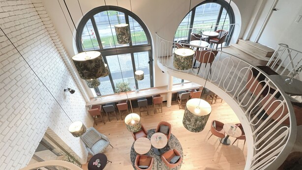 A spacious, modern interior with a central seating area, multiple tables, and a spiral staircase. - Hotel Berliner Hof by Coffee Fellows Hotels (Kiel)