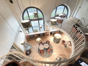 A spacious, modern interior with a central seating area, multiple tables, and a spiral staircase. - Hotel Berliner Hof by Coffee Fellows Hotels (Kiel)