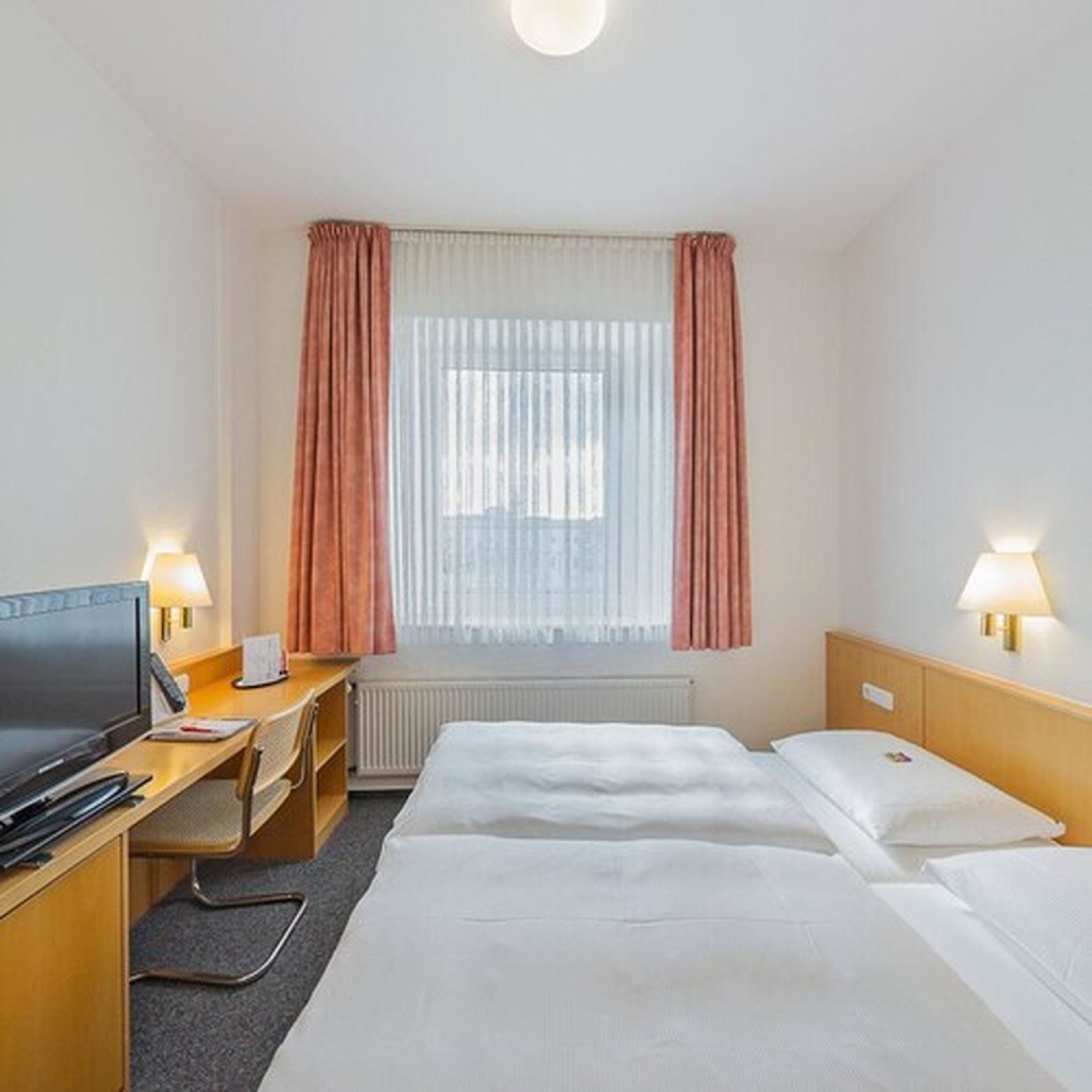 Habitación de hotel con dos camas, un escritorio, un televisor y una ventana con cortinas.