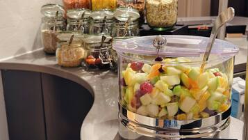 A buffet counter with a fruit salad container and various jars of condiments.