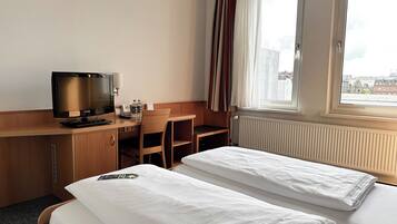 Una habitación de hotel con cama, escritorio con televisor y ventana con cortinas.