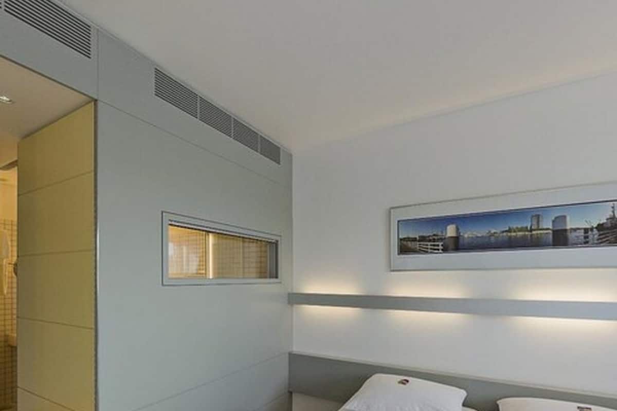 Ein modernes Hotelzimmer mit einem Bett, einem Fenster und einem Stadtbild an der Wand.