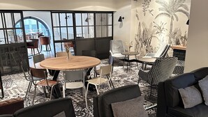 A modern interior with a round wooden table, black leather sofas, patterned chairs, and a large window with a view. - Hotel Berliner Hof by Coffee Fellows Hotels (Kiel)