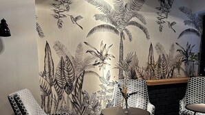 A room with patterned floor tiles, a wall mural of tropical foliage, and two chairs with a geometric pattern. - Hotel Berliner Hof by Coffee Fellows Hotels (Kiel)