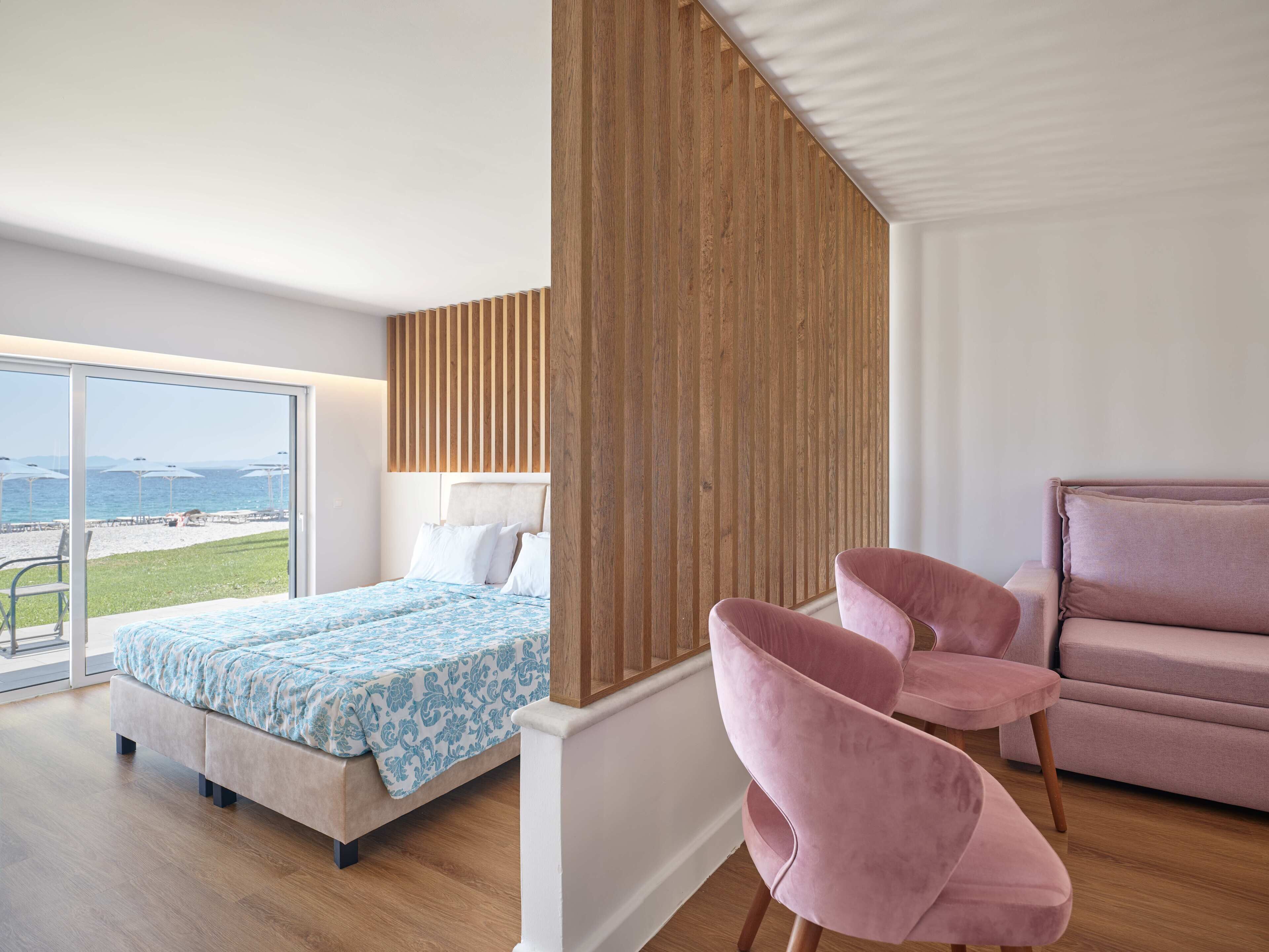 Une chambre moderne avec un lit, un fauteuil rose et une vue sur la plage.