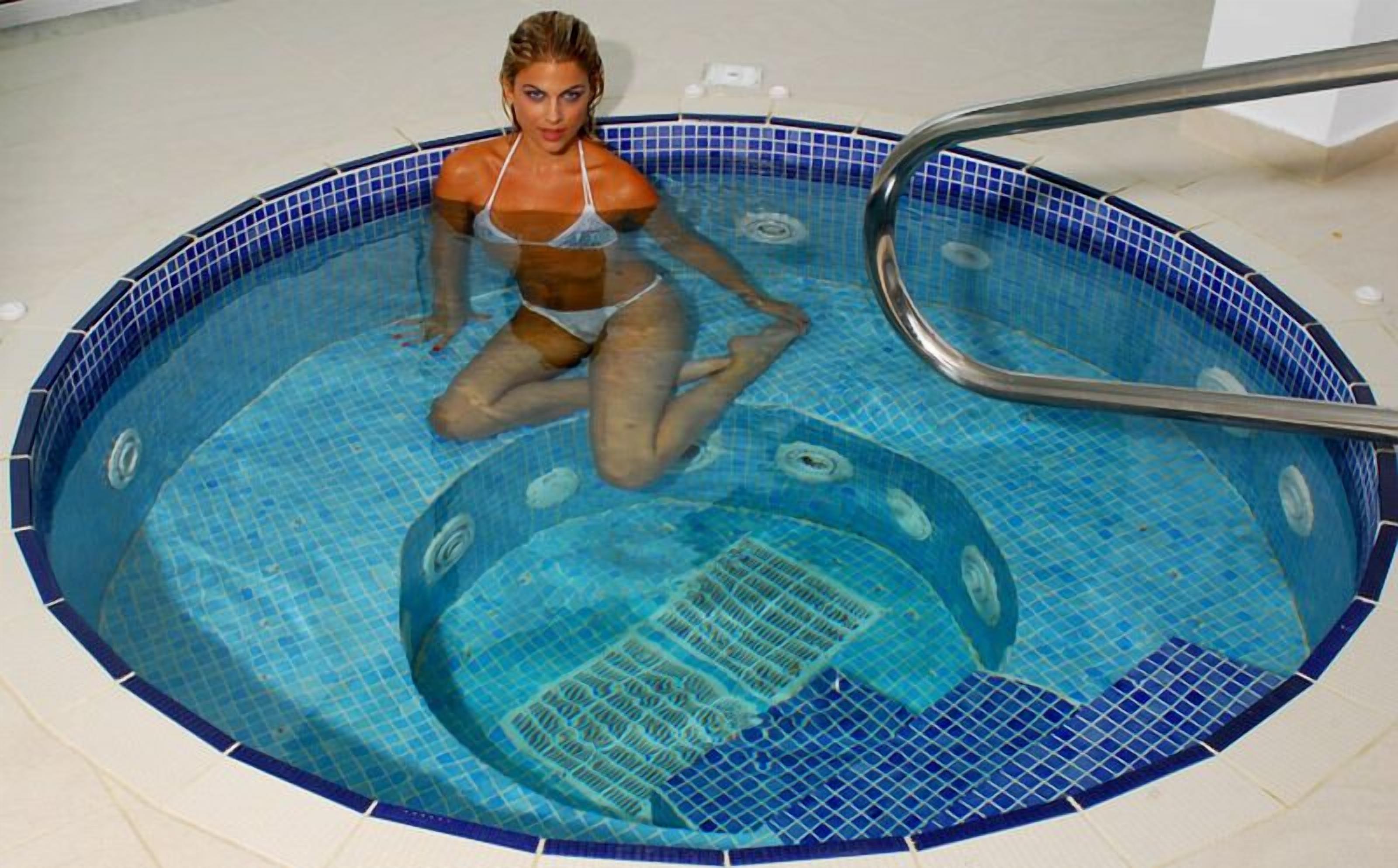 Una mujer en una piscina con borde de azulejos y una escalera de metal.