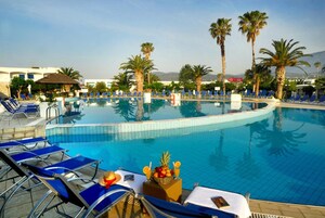 A swimming pool with blue lounge chairs, palm trees, and a mountain view.