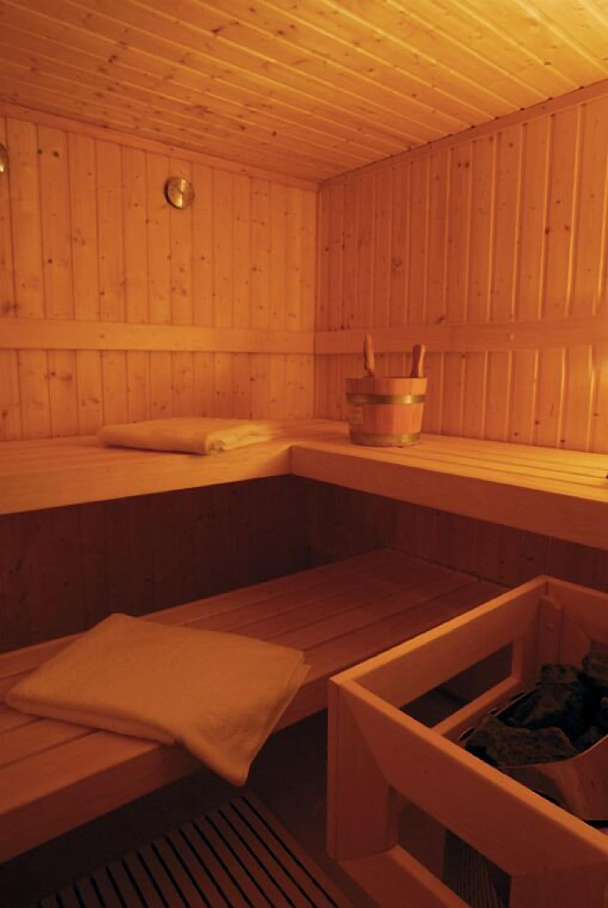 Un sauna en bois avec des bancs, un porte-serviettes et un seau contenant une brosse.