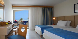A hotel room with two beds, a desk with a chair, a dining area with a table and chairs, and a view of the sea.