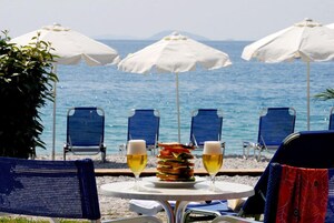 A beachside table with a plate of food and two glasses of beer, surrounded by beach chairs and umbrellas.