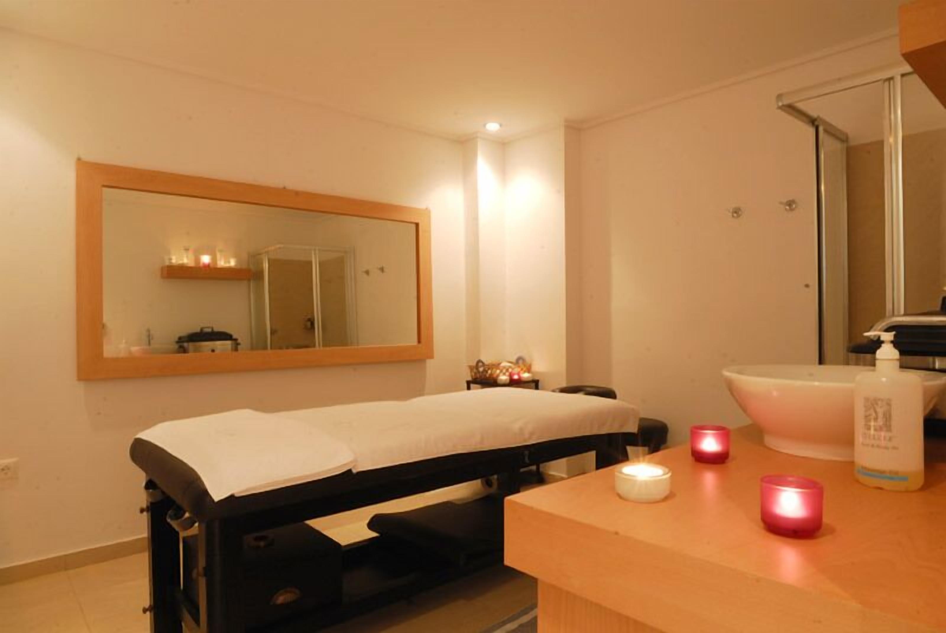 A bedroom with a single bed, a bedside table with a lamp, a mirror, and a bathroom with a sink and a large mirror.