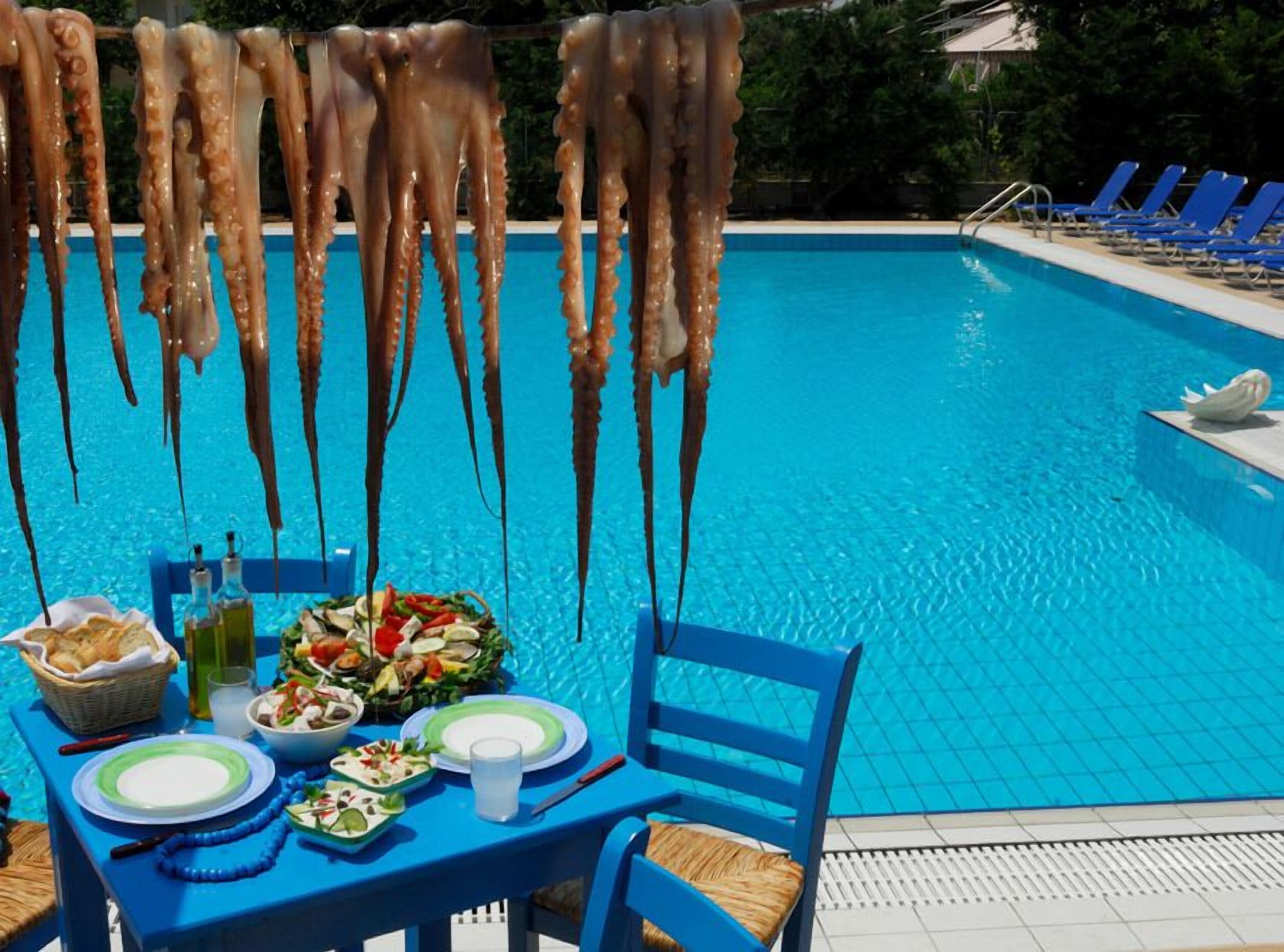 A poolside dining area with a table set for two, a variety of dishes, and hanging octopus tentacles.