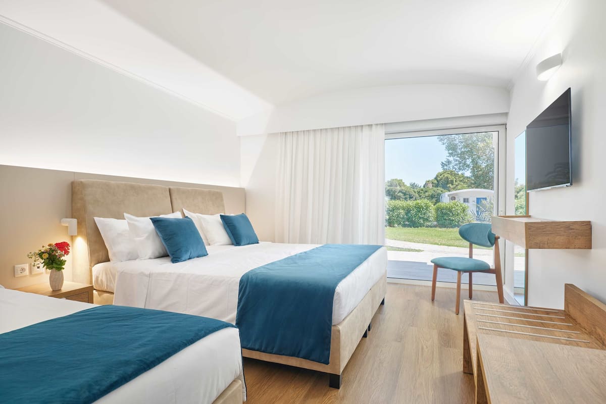 Quarto de hotel com duas camas, uma escrivaninha, uma cadeira e uma televisão.